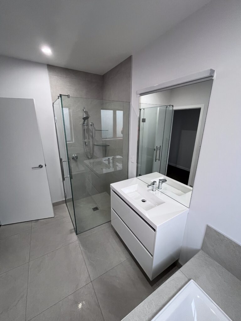 Modern bathroom with glass shower enclosure, wall-mounted fixtures and contemporary vanity unit, representing professional bathroom installation services by J. Annear Plumbing & Heating.