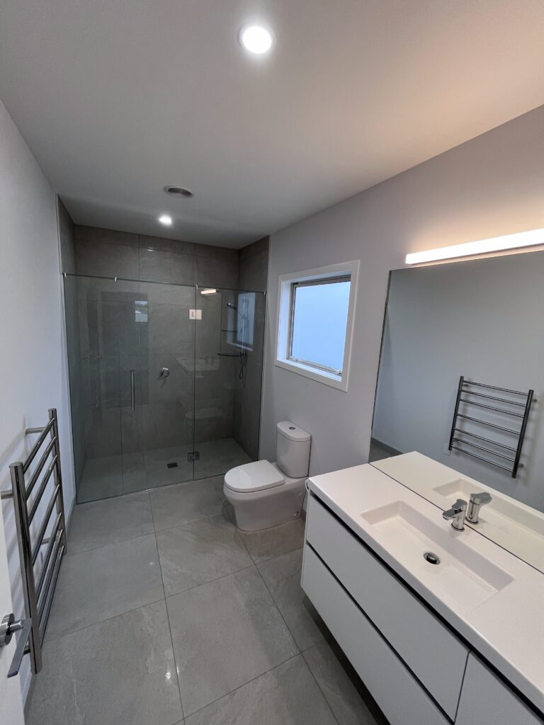 Modern bathroom with walk-in shower, fitted toilet and basin vanity, showing professional installation by J. Annear Plumbing & Heating.
