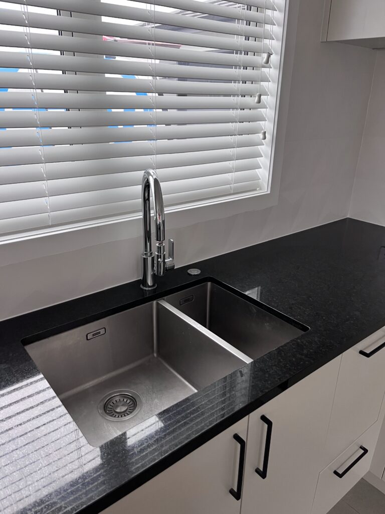 Stainless steel double kitchen sink with modern mixer tap, illustrating plumbing installation work.